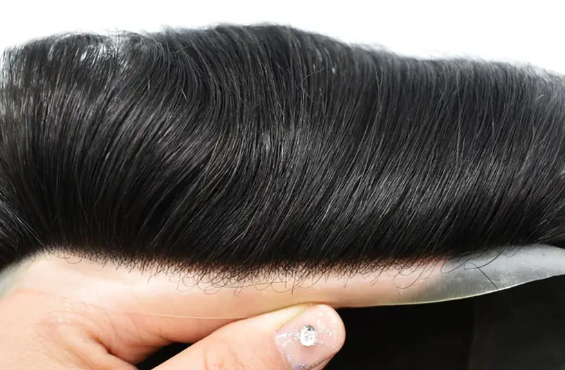 A polyurethane (skin) hair system held in one hand, showing the thin clear base edge under dark hair